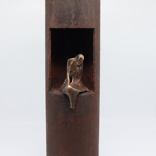 Midi urn van JEART met een bronzen beeld, geplaatst in een geroeste stalen sokkel met een messing top. De combinatie van staal, brons en messing symboliseert kracht en herinnering, en biedt een elegant en betekenisvol eerbetoon aan dierbaren.