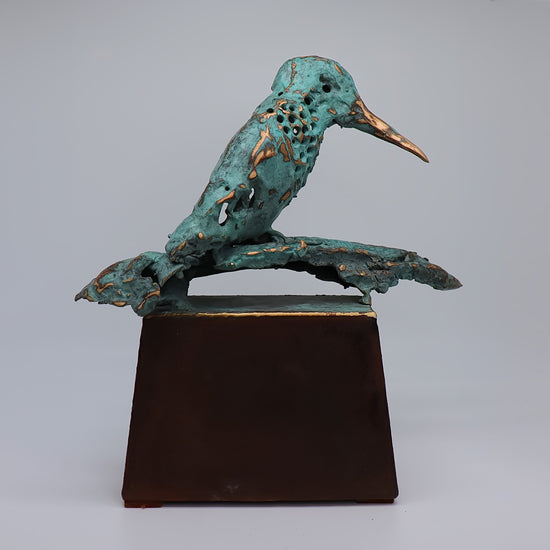 Elegante midi urn van JEART met bronzen ijsvogel rust op corten sokkel. De combinatie van duurzame materialen symboliseert kracht en eeuwigheid, terwijl de ijsvogel hoop en nieuwe beginnen vertegenwoordigt. Een stijlvolle, betekenisvolle herinnering.
